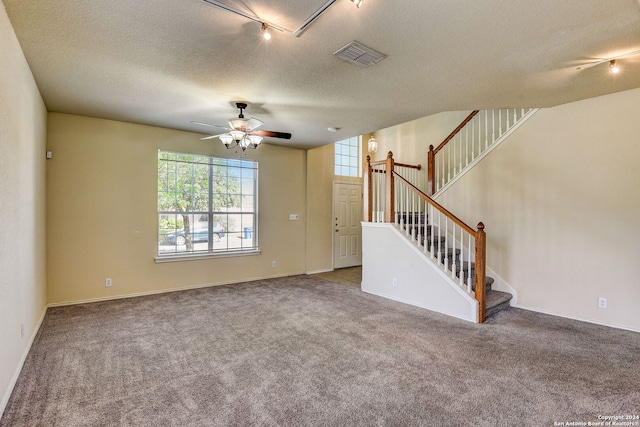 empty room featuring rail lighting, dark carpet, ceiling fan, and a textured ceiling