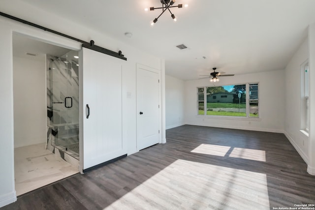 empty room with ceiling fan, a barn door, and dark tile flooring