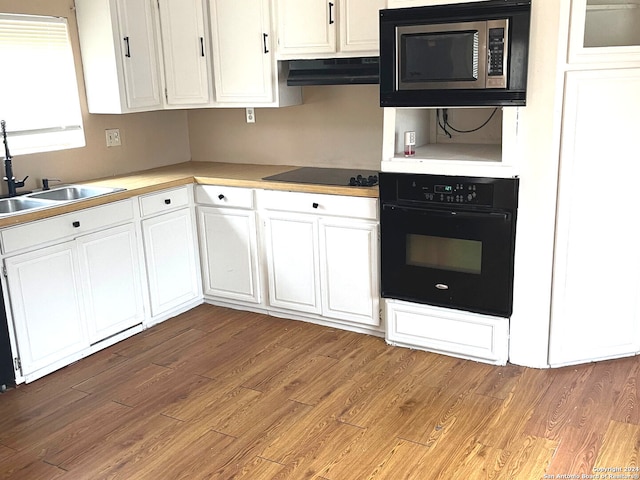 kitchen with exhaust hood, sink, light wood-type flooring, white cabinetry, and black appliances