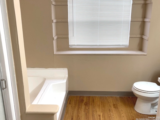 bathroom with hardwood / wood-style floors, a bath, and toilet