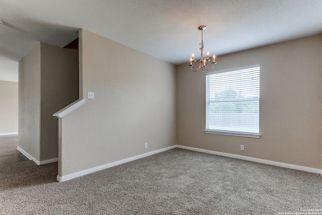 carpeted spare room with a notable chandelier and a textured ceiling