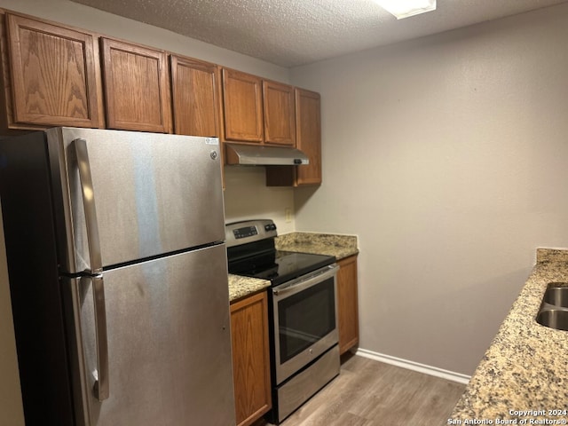 kitchen with a textured ceiling, light wood-type flooring, stainless steel appliances, and light stone countertops