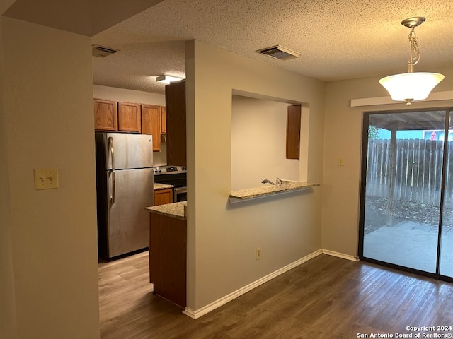 kitchen with hanging light fixtures, range with electric stovetop, a textured ceiling, stainless steel fridge, and light wood-type flooring