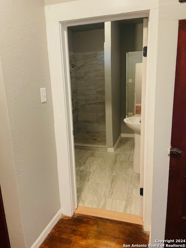 bathroom with a tile shower and wood-type flooring