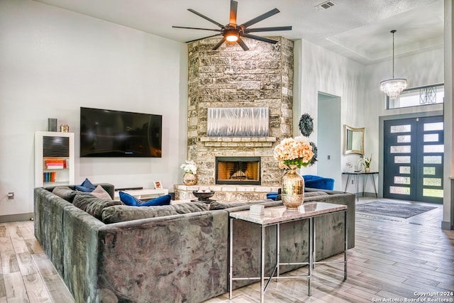 living room with light hardwood / wood-style flooring, ceiling fan with notable chandelier, and a stone fireplace