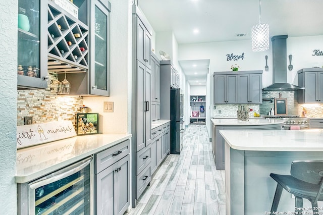 kitchen featuring a kitchen breakfast bar, wine cooler, decorative light fixtures, wall chimney range hood, and tasteful backsplash