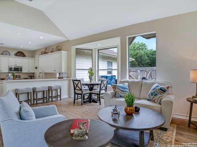 living room with light wood-type flooring, sink, and lofted ceiling