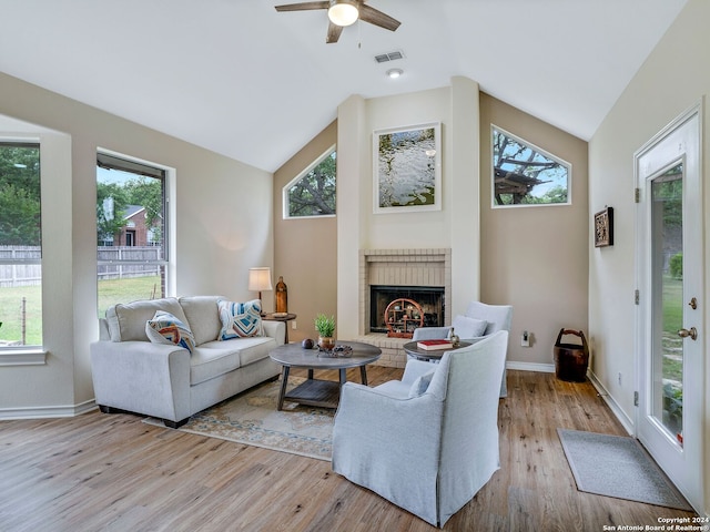 living room with high vaulted ceiling, a brick fireplace, ceiling fan, and light wood-type flooring