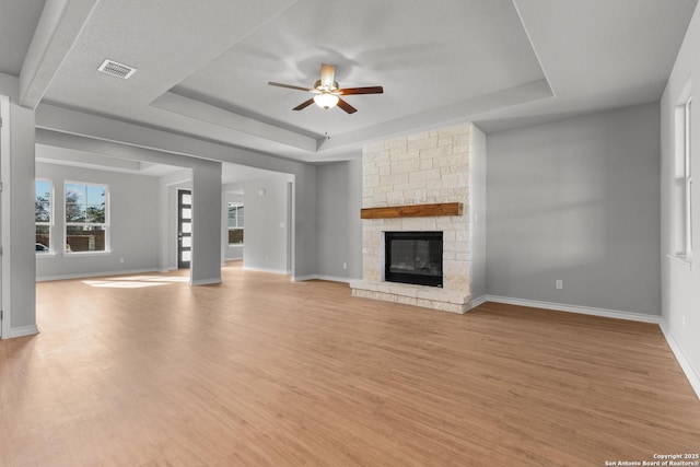 unfurnished living room featuring a fireplace, light hardwood / wood-style floors, a tray ceiling, and ceiling fan