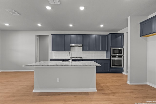 kitchen with light stone countertops, appliances with stainless steel finishes, a center island with sink, and sink