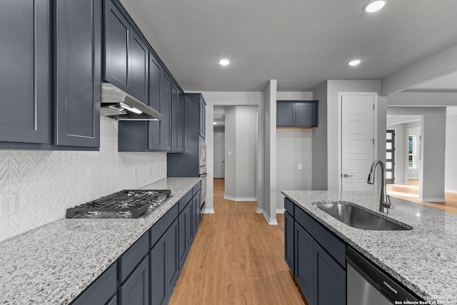 kitchen featuring tasteful backsplash, sink, light wood-type flooring, light stone countertops, and stainless steel appliances