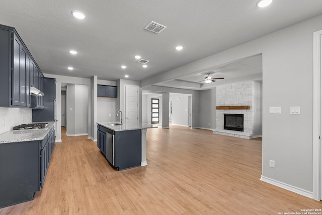 kitchen featuring light hardwood / wood-style floors, sink, a kitchen island with sink, and a stone fireplace