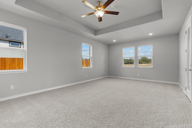 carpeted empty room with ceiling fan and a tray ceiling