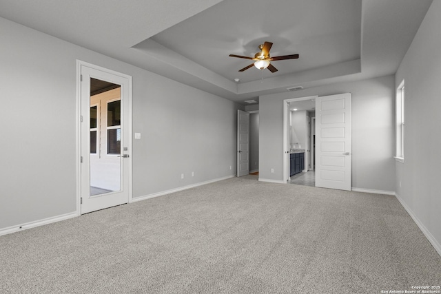 unfurnished bedroom featuring a raised ceiling, ceiling fan, carpet floors, and connected bathroom