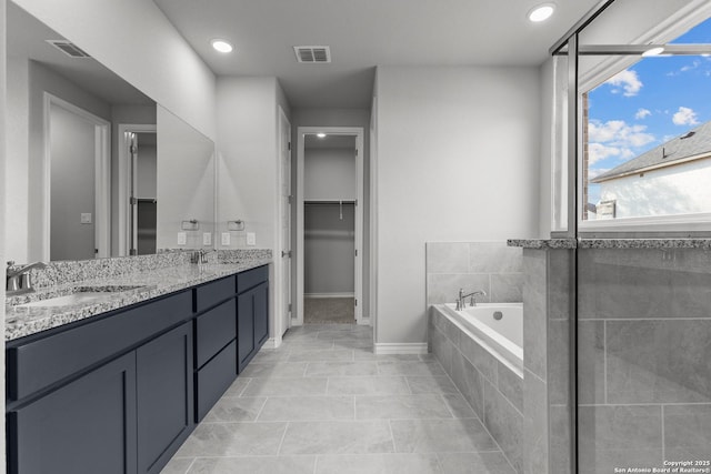 bathroom with tiled bath, vanity, and tile patterned flooring