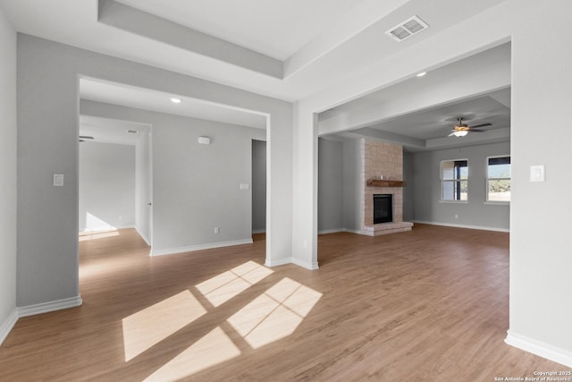 unfurnished living room with ceiling fan, light hardwood / wood-style flooring, a raised ceiling, and a fireplace