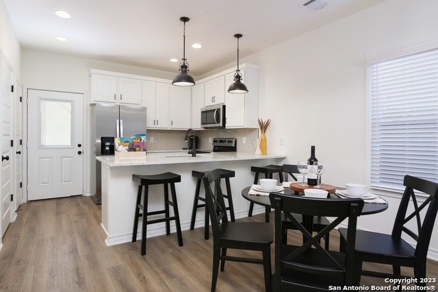 kitchen with wood-type flooring, appliances with stainless steel finishes, kitchen peninsula, and white cabinetry