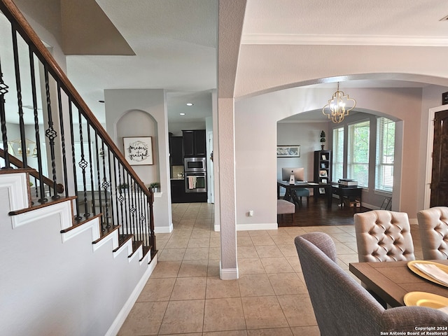 tiled foyer entrance with ornamental molding and an inviting chandelier