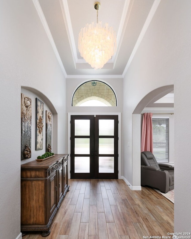 foyer entrance featuring french doors, a tray ceiling, ornamental molding, an inviting chandelier, and hardwood / wood-style flooring