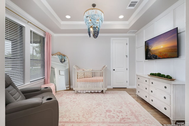 bedroom featuring ornamental molding, wood-type flooring, a nursery area, and a raised ceiling