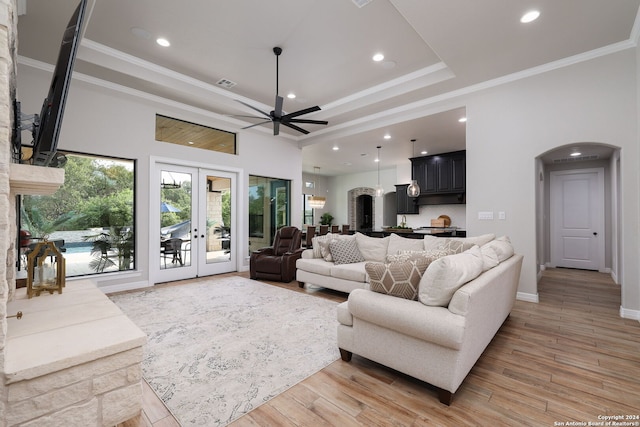 living room featuring ceiling fan, light hardwood / wood-style floors, a raised ceiling, crown molding, and french doors