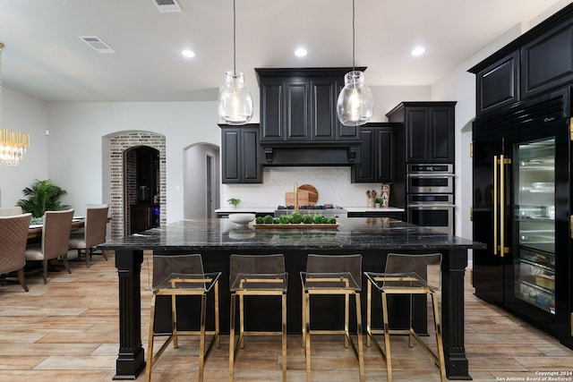 kitchen featuring hanging light fixtures, light wood-type flooring, appliances with stainless steel finishes, tasteful backsplash, and exhaust hood