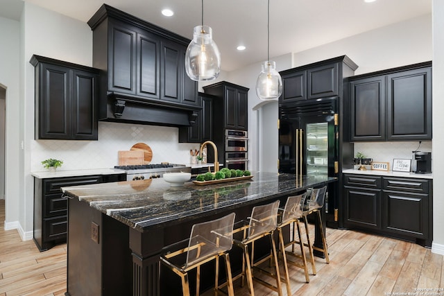 kitchen with light hardwood / wood-style flooring, tasteful backsplash, a center island with sink, and extractor fan