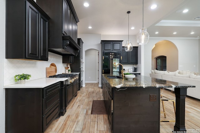 kitchen featuring backsplash, a breakfast bar area, a kitchen island with sink, light wood-type flooring, and ornamental molding