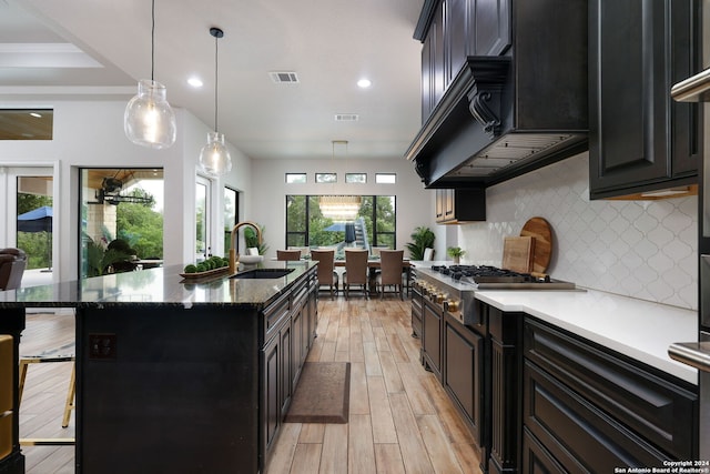 kitchen featuring hanging light fixtures, light hardwood / wood-style floors, backsplash, and a kitchen island with sink