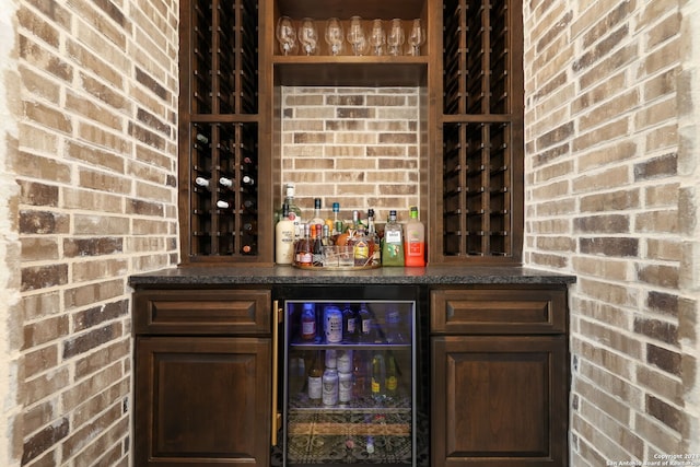 interior space featuring beverage cooler, dark brown cabinets, and brick wall