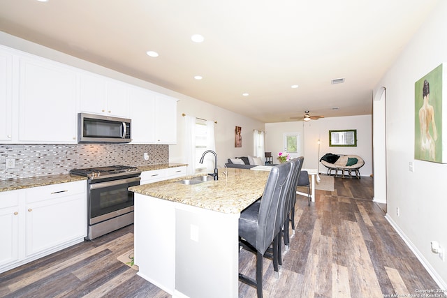 kitchen with sink, backsplash, hardwood / wood-style floors, stainless steel appliances, and an island with sink