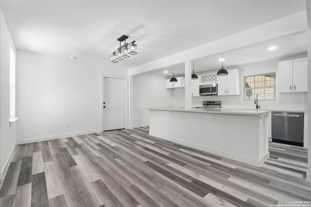 kitchen with appliances with stainless steel finishes, white cabinets, sink, hanging light fixtures, and hardwood / wood-style flooring