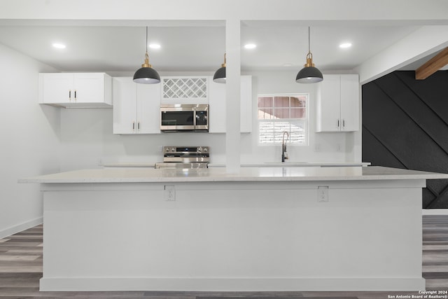 kitchen with appliances with stainless steel finishes, wood-type flooring, hanging light fixtures, and white cabinets