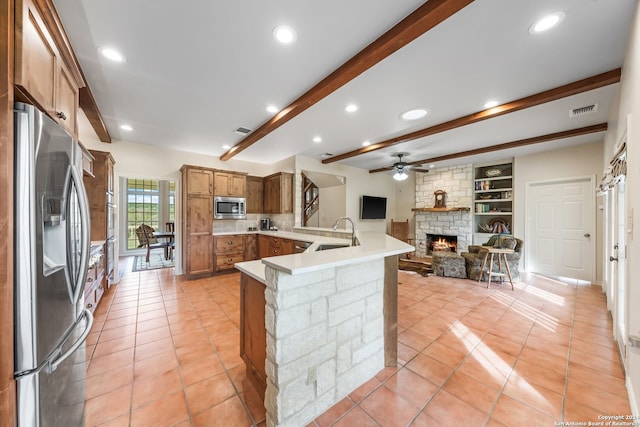 kitchen with kitchen peninsula, stainless steel appliances, beamed ceiling, a fireplace, and light tile floors