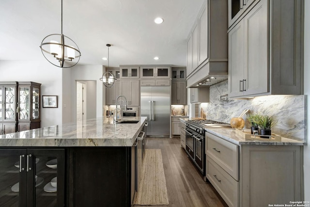 kitchen featuring decorative light fixtures, a large island with sink, sink, high end appliances, and light stone counters