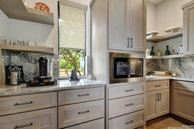 kitchen with decorative backsplash, light stone countertops, light hardwood / wood-style flooring, and built in microwave