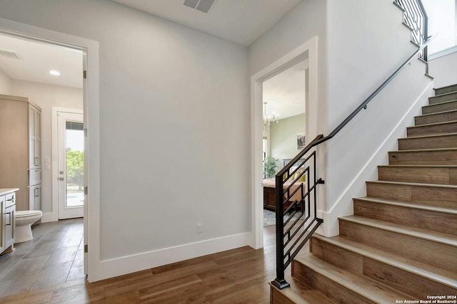 stairway with wood-type flooring and an inviting chandelier