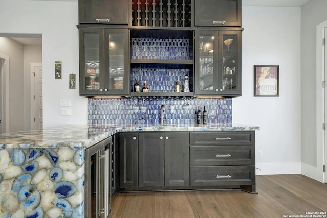 bar featuring tasteful backsplash, hardwood / wood-style floors, sink, light stone countertops, and beverage cooler