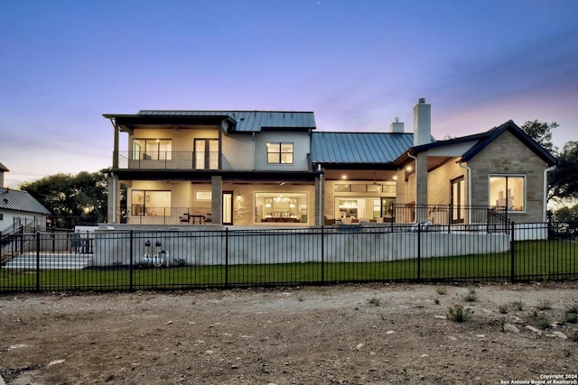 back house at dusk with a lawn and a balcony