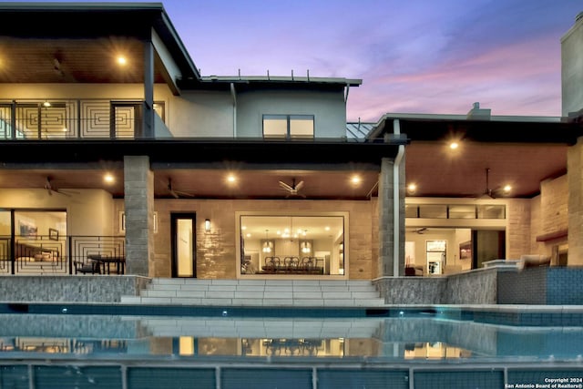 back house at dusk featuring ceiling fan and a balcony