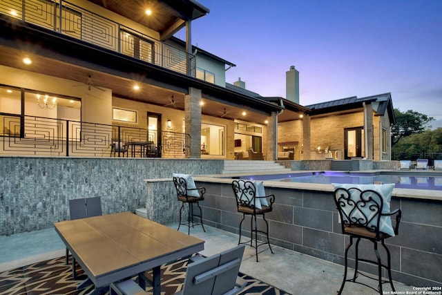 patio terrace at dusk featuring ceiling fan and an outdoor bar