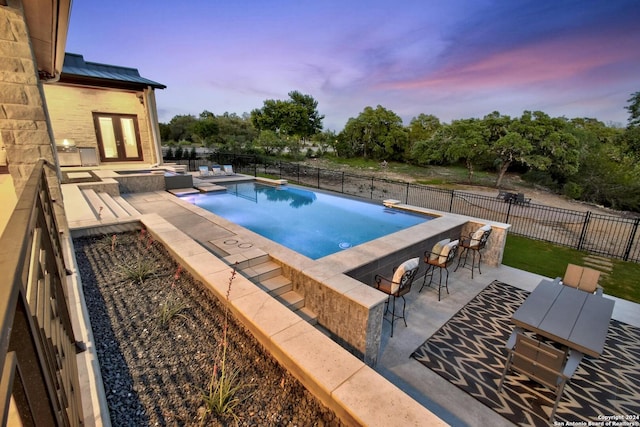 pool at dusk with a patio area, an outdoor bar, a hot tub, and french doors