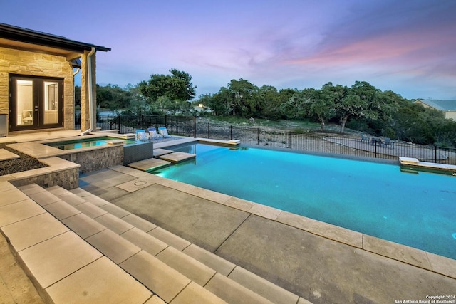 pool at dusk featuring french doors, a patio area, and an in ground hot tub