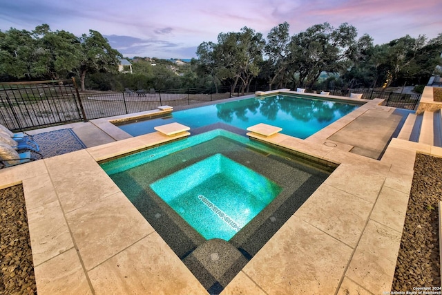 pool at dusk with an in ground hot tub