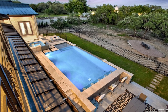 pool at dusk featuring an outdoor fire pit, a patio area, a yard, and an in ground hot tub