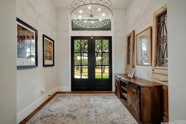 foyer entrance featuring a chandelier, wood-type flooring, a towering ceiling, and french doors