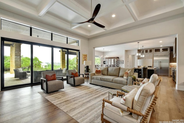 living room featuring light hardwood / wood-style floors, coffered ceiling, a towering ceiling, ceiling fan with notable chandelier, and beamed ceiling