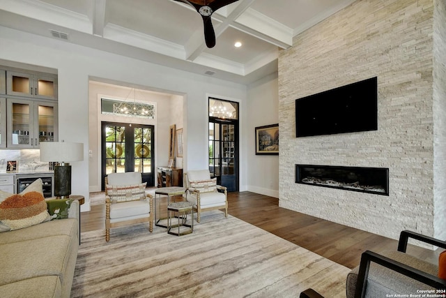 living room featuring hardwood / wood-style flooring, coffered ceiling, a stone fireplace, french doors, and beam ceiling