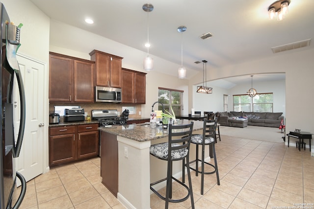 kitchen featuring black refrigerator, stove, a breakfast bar, a center island with sink, and vaulted ceiling