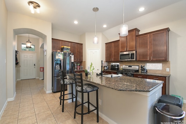 kitchen with a kitchen breakfast bar, decorative light fixtures, appliances with stainless steel finishes, a center island with sink, and tasteful backsplash